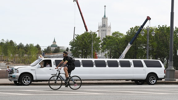 Eine weiße Stretchliimousine steht auf der Grossen Moskauer Bruecke und wartet auf eine Hochzeitsgesellschaft, die sich vor der Kreml Kulisse fotografieren laesst. Davor ein Fahrradfahrer.