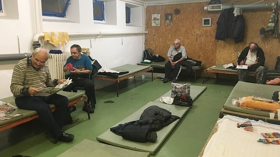 Männer in einer Notunterkunft für Obdachlose sitzen auf ihren Pritschen