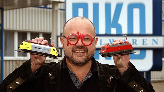 PIKO Chef Dr. Rene F. Wilfer, mit seiner markanten piko-Brille, posiert mit zwei Modell-Triebwagen seiner Firma.
