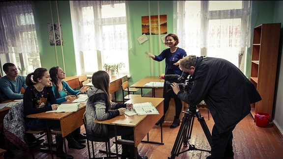 Ein Mann mit einer Kamera filmt in einem vollbesetzten Klassenzimmer.