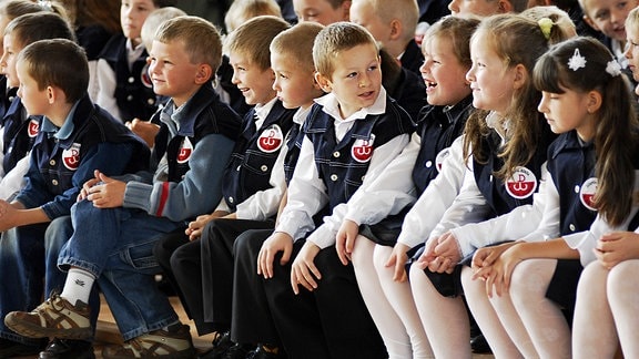 Lachende polnische Kinder in Schuluniform bei der Einschulungsfeier.