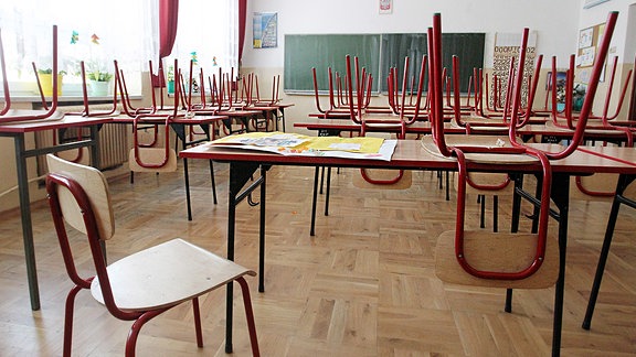 Ein leeres Klassenzimmer. Die Stühle sind auf die Bänke gestellt.