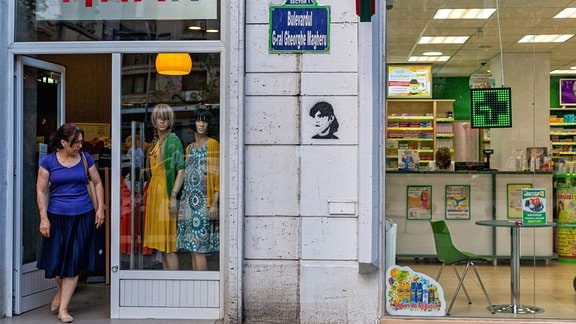 Straßenszene in Bukarest. Eine Frau verlässt einen Laden. Das Graffiti an der Häuserwand in Bukarest zeigt die rumänische Staatsanwältin Laura Codruta Kövesi.