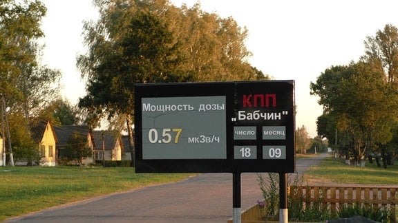 Schild mit kyrillisch geschriebenen Daten zur Strahlenbelastung an einer Straße. Im Hintergrund einige Häuser.