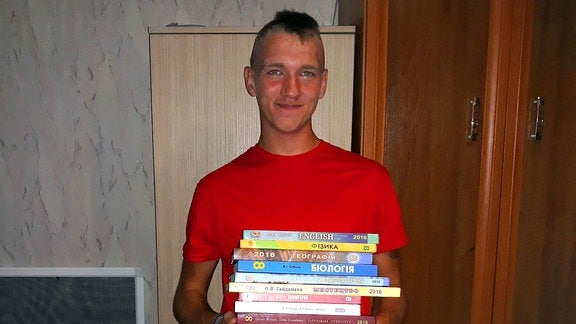 Blonder junge in rotem Shirt hält Stapel mit ukrainischen Schulbüchern