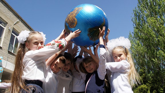 Sechs Mädchen halten eine Erdkugel aus Gummi hoch in die Luft