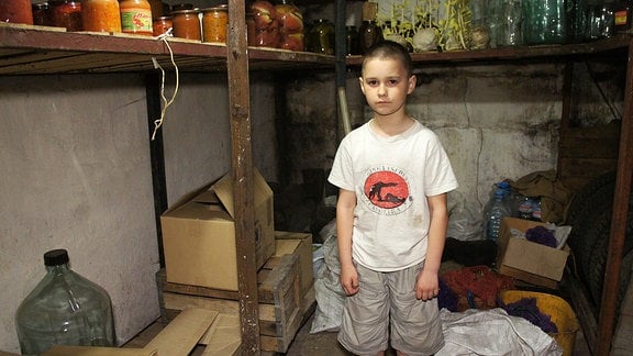 Kleiner Junge steht in einem Keller. In Regalen gefüllte Einweckgläser.