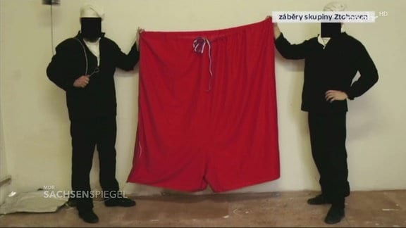 Zwei maskierte Männer halten eine sehr große Unterhose.