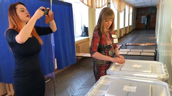 Eine Frau macht mit einem Smartphone ein Foto von Wahlurnen
