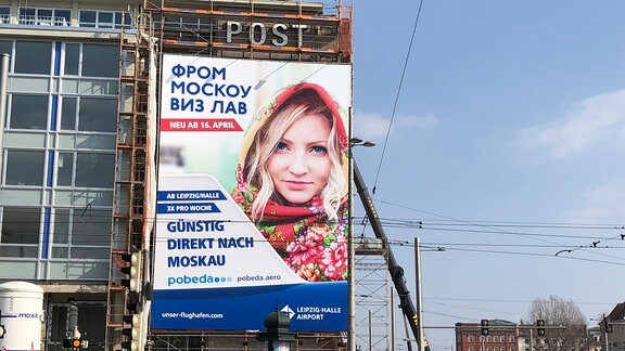 Pobeda-Werbeplakat am Leipziger Augustusplatz. Darauf steht in kyrillischer Umschrift From Moscou wiz law