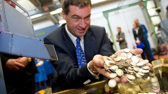 Markus Söder (CSU), wühlt einer Kiste mit 2-Euromünzen