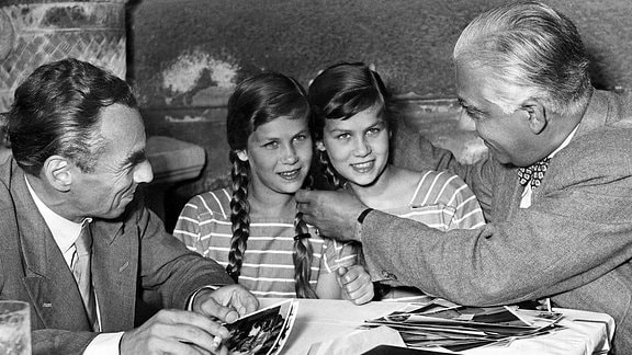 Schwarz-Weiß-Fotografie: Zwillingsmädchen, links und rechts von ihnen sitzt ein älterer Mann im Anzug.