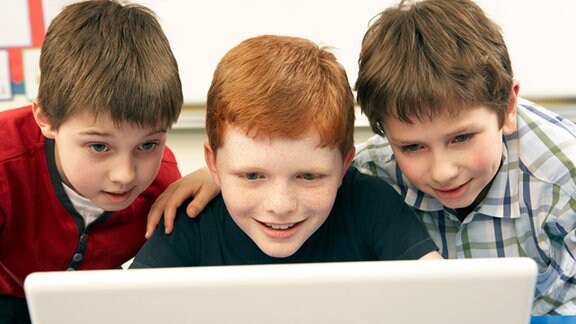 Drei Jungs starren gespannt auf einen Monitor.