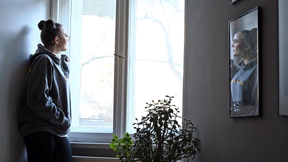 Eine junge Frau steht allein am Fenster und schaut hinaus.