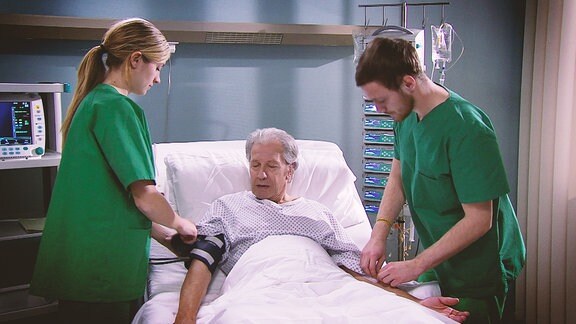 Ein älterer Herr wir in seinem Krankenbett von einer Krankenschwester und einem Krankenpfleger untersucht.