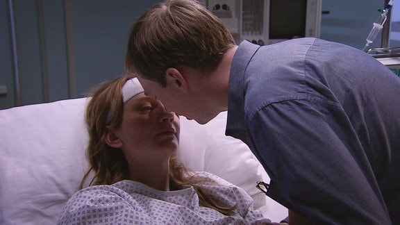Eine junge Frau liegt mit einer Kopfverletzung im Krankenbett. Ihr bester Freund gesteht ihr seine Liebe und beugt sich über sie, um sie zu küssen.