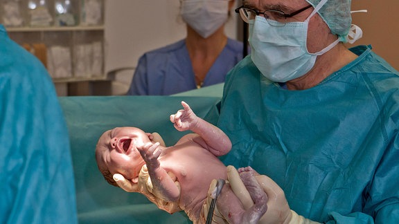 Ein Arzt hält in einem Kreissaal ein Neugeborenes in den Händen