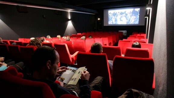 Menschen sitzen in einem noch erleuchteten Kinosaal