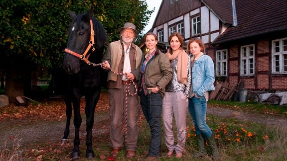 Matthiesen steht mit seinen Töchtern und einem Pferd vor einem Haus