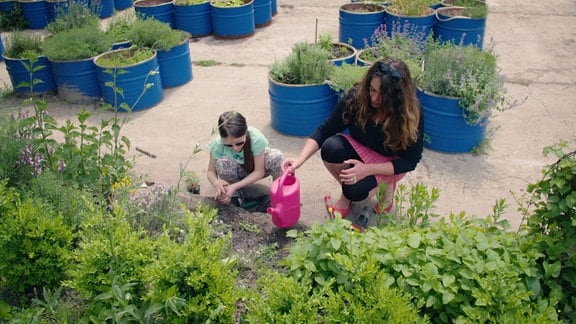 Eine junge Frau ist mit ihrer Tochter in einem urbanen Stadtgarten und gießt Pflanzen