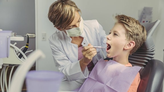 Eine Zahnärztin schaut einem Jungen bei einer Zahnvorsorge in den Mund
