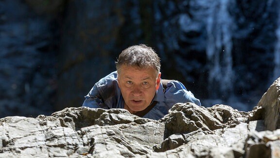 Dr. Roland Heilmann (Thomas Rühmann) klettert einen Felsen hoch