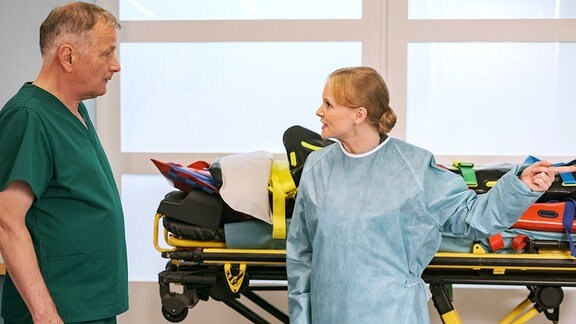 Dr. Heilmann und eine Besucherin in blauem Kittel stehen in einem Behdandlungsraum. 