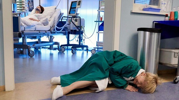 Dr. Kathrin Globisch (Andrea Kathrin Loewig, vorn) krümmt sich am Boden vor einem Patientenzimmer.