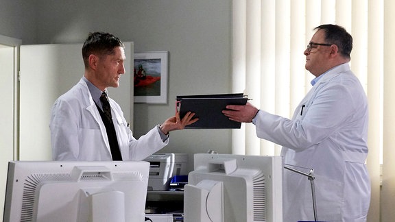 Dr. Kaminski (Udo Schenk, li.) überreicht Hans-Peter Brenner (Michael Trischan, re.) in einem Büro eine Patientenakte