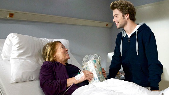 Kris Haas (Jascha Rust) steht am Krankenbett von Regina Ströwe (Veronika Nowag-Jones).