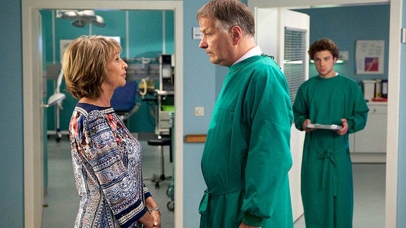 Barbara Grigoleits (Uta Schorn, li.) und Dr. Roland Heilmann (Thomas Rühmann, mi.) stehen sich im Krankenhausflur gegenüber.