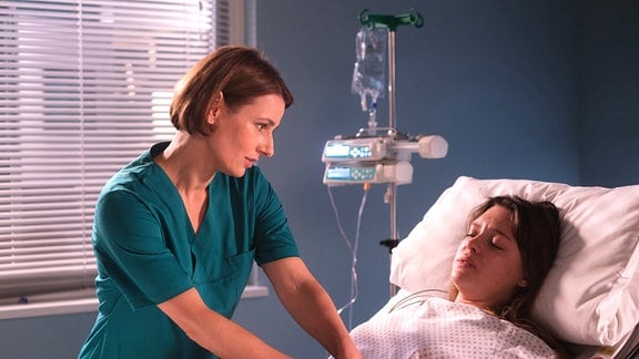 Eine Frau untersucht eine junge Frau im Krankenbett