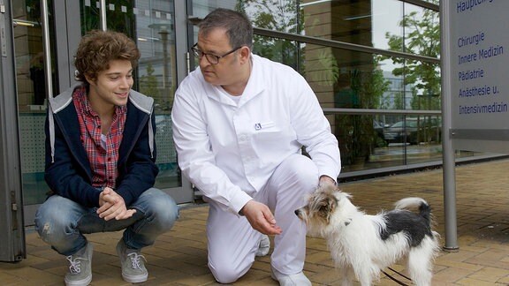 Hans-Peter Brenner (Michael Trischan, re.) und Kris Haas (Jascha Rust, li.) mit einem Hund vor der Klinik.