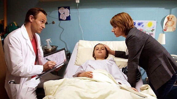 Kilian liegt im Krankenbett, seine Mutter und Dr. Stein stehen bei ihm.