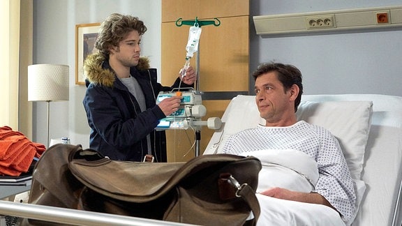 Durch Simon Haas (Tom Mikulla, re.) Krankenhausaufenthalt sind er und sein Sohn Kris (Jascha Rust, li.) das erste Mal seit Langem wieder zu Gesprächen gezwungen.