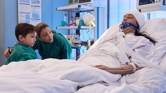 Karim Jandali (Mamaar Abbou) steht mit Schwester Arzu am Bett seiner Schwester.