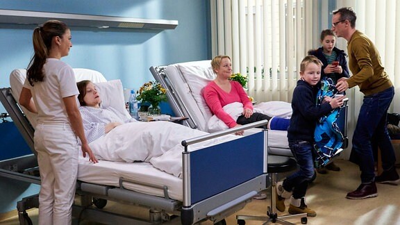 Jessika Wendel teilt sich das Krankenzimmer mit Vollblutmutter Silke Bluhm, die gerade Besuch ihres Mannes Thomas und ihrer drei Kinder hat. Arzu mahnt zur Ruhe