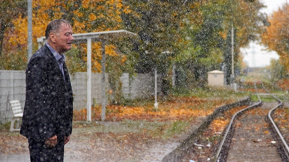 Ein Mann neben Bahngleisen. Es schneit. 