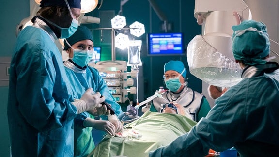 Dr. Lilly Phan (Mai Duong Kieu, 2.v.li.) operiert Resa Niebur (Emma Bahlmann, liegend), neben ihr Dr. Martin Stein (Bernhard Bettermann, li.).