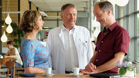 Roland Heilmann (Thomas Rühmann, mi.) trifft in der Cafeteria seinen alten Freund Achim (Holger Daemgen, re.) und seine Freundin Katja (Julia Jäger, li.).