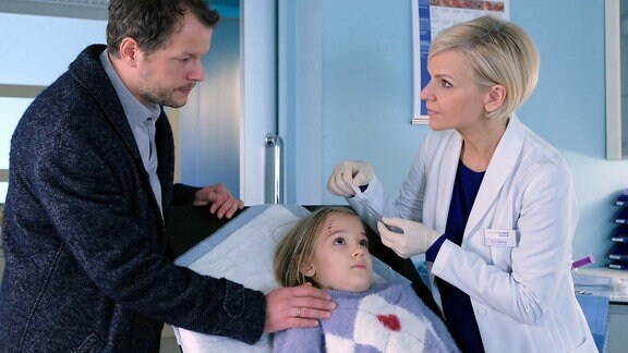 Tom Wolter (Mirko Lang, li.) bringt seine sechsjährige Tochter Clara (Elisabeth Lattner, mi.) in die Sachsenklinik. Dr. Kathrin Globisch (Andrea Kathrin Loewig, re.) untersucht sie.