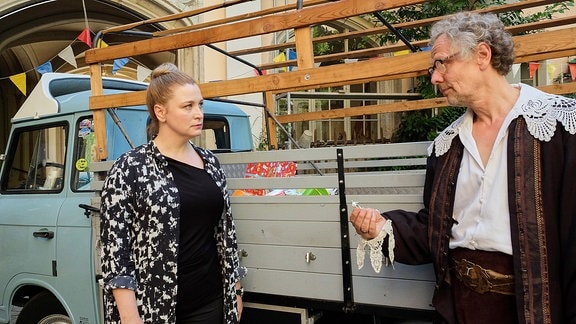 Ein Mann spricht mit einer jungen Frau vor einem alten Bus. 