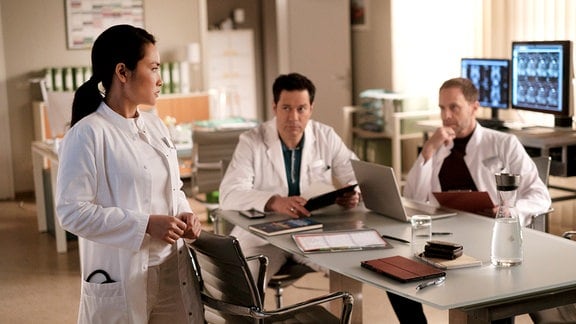 Dr. Brentano (Thomas Koch, mi.), Dr. Hoffmann (Julian Weigend, re.) und Dr. Lilly Phan (Mai Duong Kieu, li.) im Ärztezimmer.