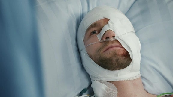 Ein Patient liegt im Krankenbett mit verbundenem Kopf.