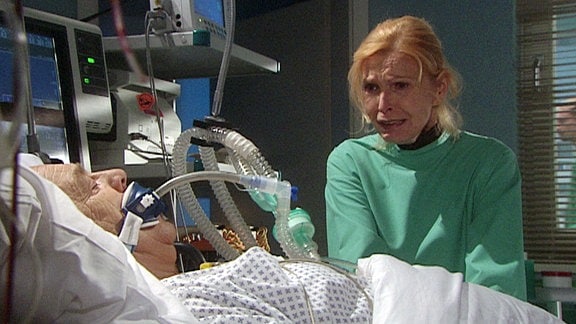 Eine Frau weint am Krankenbett eines Mannes.
