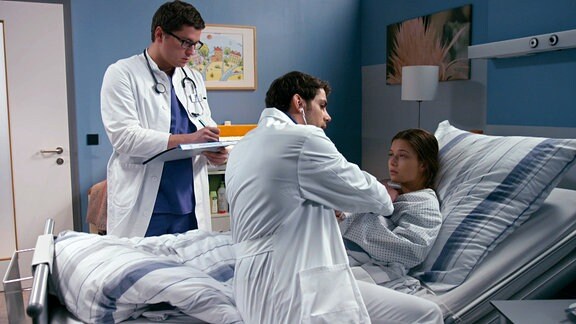 Zwei Mediziner untersuchen eine Frau in einem Krankenbett.