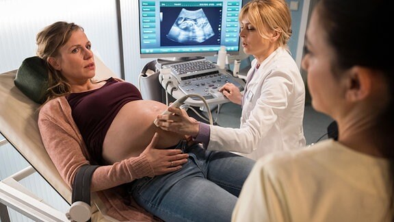 Lana Moschs (Katrin Jaehne, li.) Geburtstermin ist seit einer Woche überfällig. Dr. Ina Schulte (Isabell Gerschke, mi.) und Schwester Arzu (Arzu Bazman, re.) betreuen sie nun engmaschig. Doch irgendetwas verhindert Lanas Vorfreude auf das Baby.