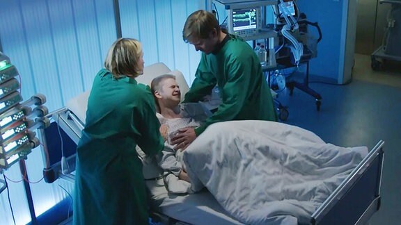 Patient liegt im Bett und wird von Ärzten versorgt