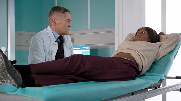 Serie: "In aller Freundschaft": Ein Arzt sitzt vor einer Patientin auf einer Liege.
