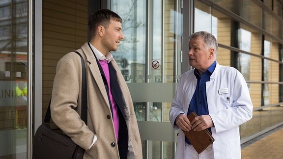 Dr. Roland Heilmann (Thomas Rühmann, re.) findet es ziemlich unangebracht, dass Lukas Globisch (Frederik Götz, li.) vor der Klinik Beziehungsratschläge verteilt.